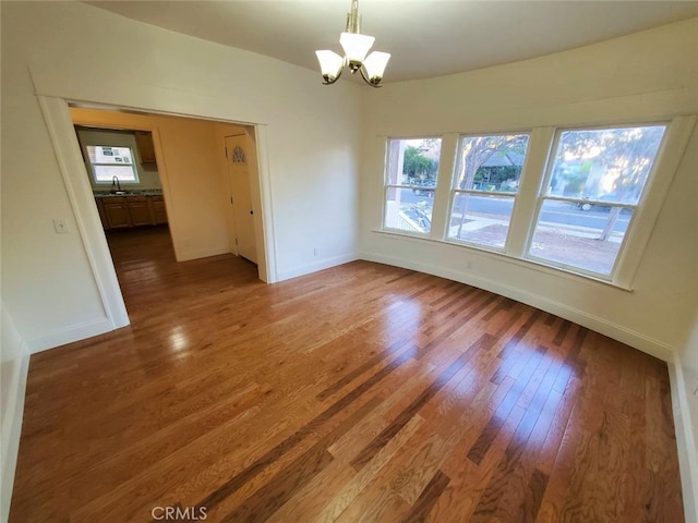 unfurnished room featuring wood-type flooring, sink, and an inviting chandelier