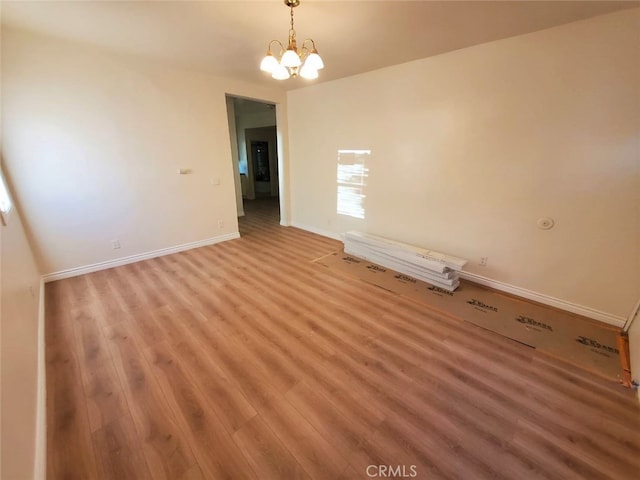 empty room with wood-type flooring and a chandelier