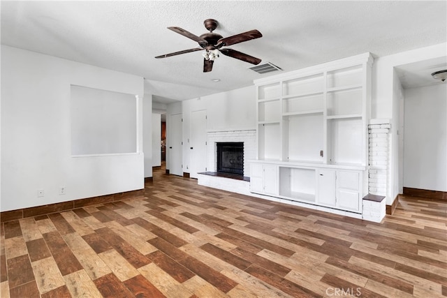 unfurnished living room featuring ceiling fan, hardwood / wood-style flooring, a fireplace, and a textured ceiling