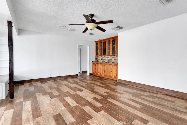 unfurnished living room with a textured ceiling, wood-type flooring, and ceiling fan