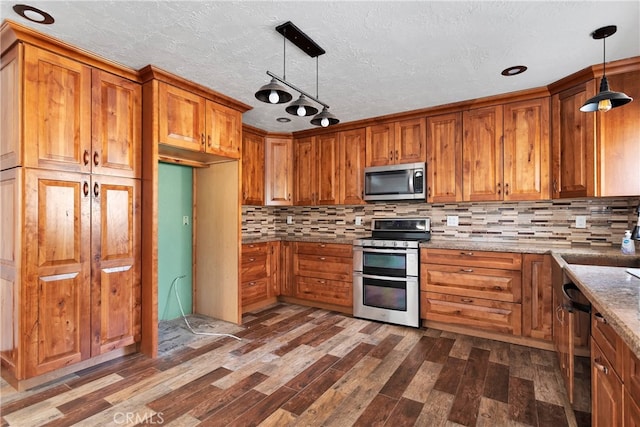 kitchen with light stone countertops, appliances with stainless steel finishes, pendant lighting, and dark wood-type flooring