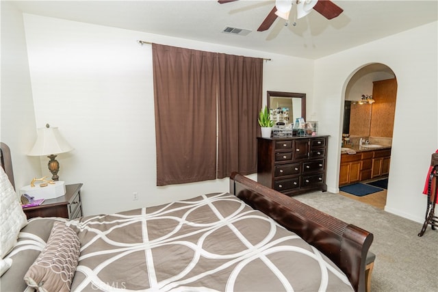 bedroom with ceiling fan, sink, light carpet, and ensuite bath