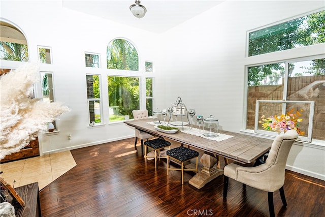 dining area featuring a healthy amount of sunlight, dark wood-type flooring, and a high ceiling