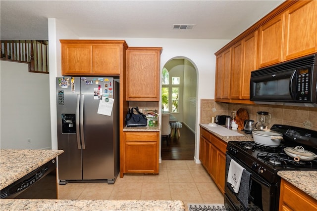 kitchen with decorative backsplash, light tile patterned floors, light stone counters, and black appliances