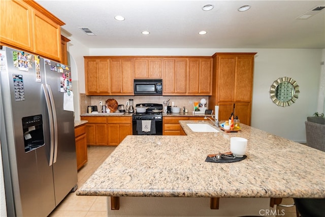 kitchen with black appliances, sink, decorative backsplash, light tile patterned floors, and an island with sink