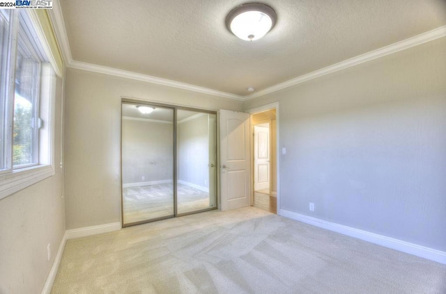 unfurnished bedroom featuring a textured ceiling, ornamental molding, light carpet, and a closet