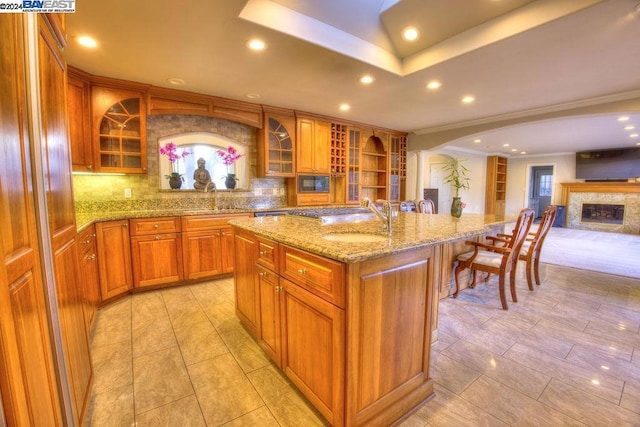 kitchen featuring sink, decorative backsplash, light stone counters, and a kitchen island with sink