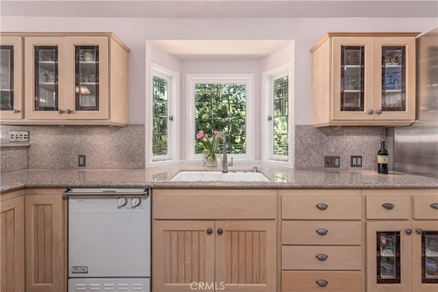 kitchen with decorative backsplash, light brown cabinets, stainless steel dishwasher, and sink