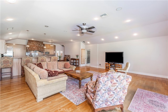 living room with ceiling fan, light hardwood / wood-style floors, and vaulted ceiling