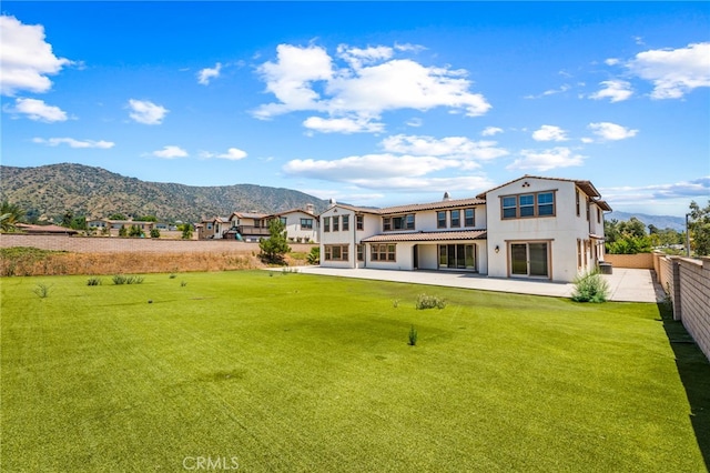 back of property featuring a mountain view, a patio, and a lawn