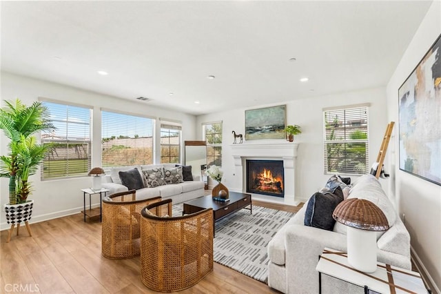 living room featuring a warm lit fireplace, light wood-type flooring, visible vents, and baseboards