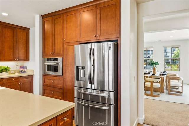 kitchen with carpet, light countertops, appliances with stainless steel finishes, and brown cabinetry