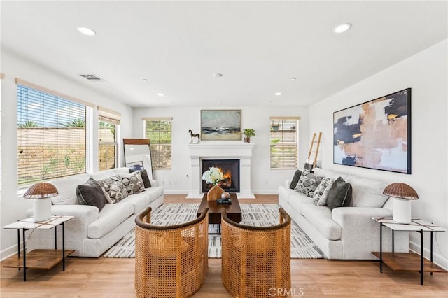 living room with a lit fireplace, visible vents, light wood-style flooring, and recessed lighting