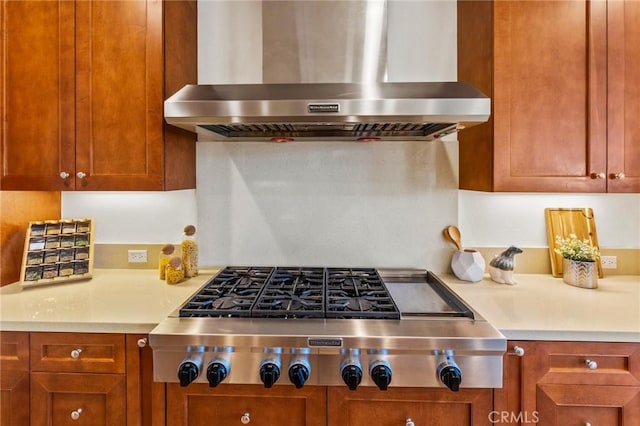 kitchen with stainless steel gas stovetop, light countertops, wall chimney exhaust hood, and brown cabinetry