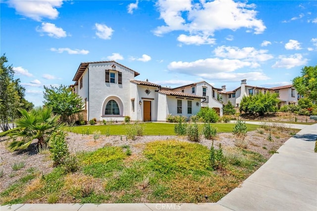 mediterranean / spanish home with a tiled roof, stucco siding, and a front lawn