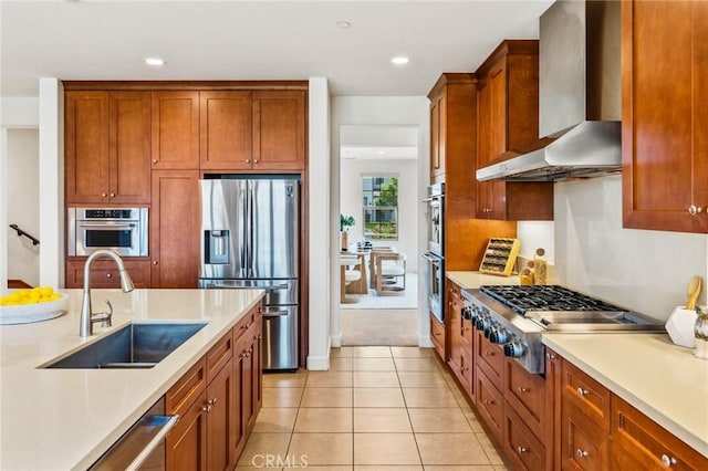 kitchen featuring light tile patterned flooring, light countertops, a sink, stainless steel appliances, and wall chimney range hood