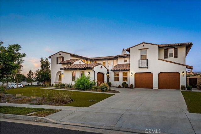 mediterranean / spanish-style house featuring a tiled roof, concrete driveway, stucco siding, and a front lawn