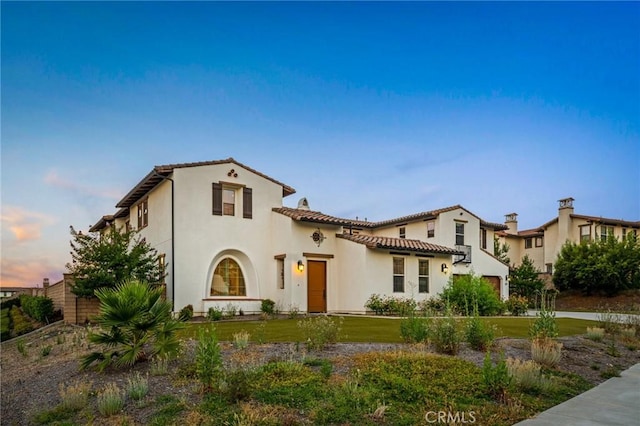 mediterranean / spanish home with driveway, fence, a tiled roof, stucco siding, and a yard