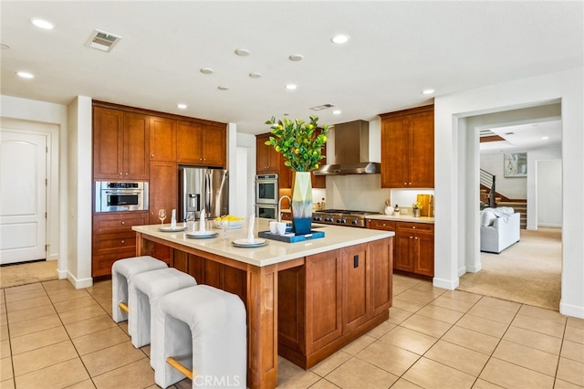 kitchen with a kitchen breakfast bar, wall chimney exhaust hood, stainless steel appliances, light colored carpet, and a kitchen island with sink