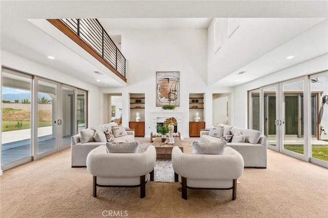 carpeted living area featuring built in features, a fireplace, french doors, and a towering ceiling