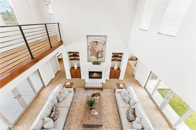 carpeted living area with a lit fireplace and a high ceiling