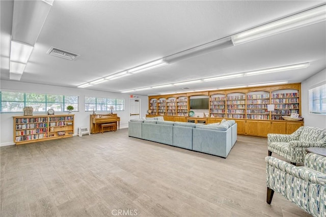 unfurnished living room with bookshelves, light wood-type flooring, visible vents, and baseboards