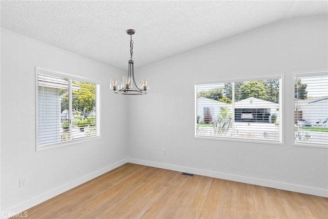 spare room with a chandelier, a textured ceiling, visible vents, baseboards, and light wood-style floors