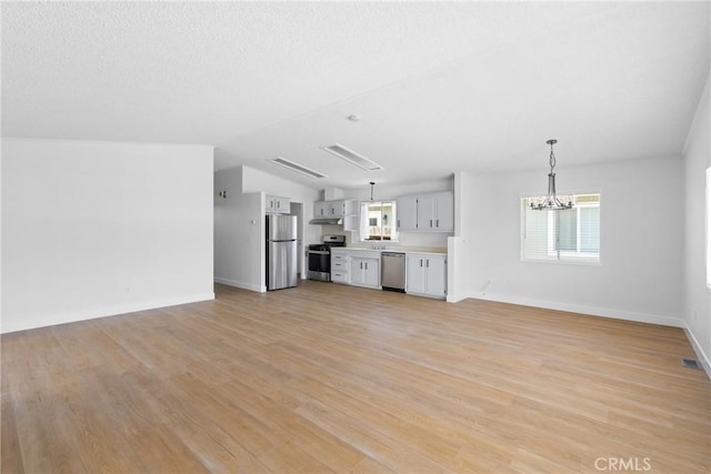 unfurnished living room featuring a chandelier, a healthy amount of sunlight, lofted ceiling, and light wood-style floors