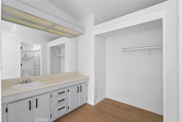 full bathroom featuring toilet, a textured ceiling, vanity, wood finished floors, and baseboards