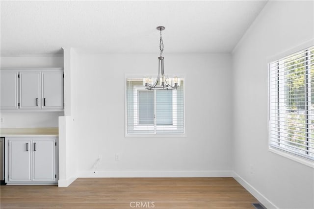 unfurnished dining area featuring plenty of natural light, light wood-style flooring, baseboards, and an inviting chandelier