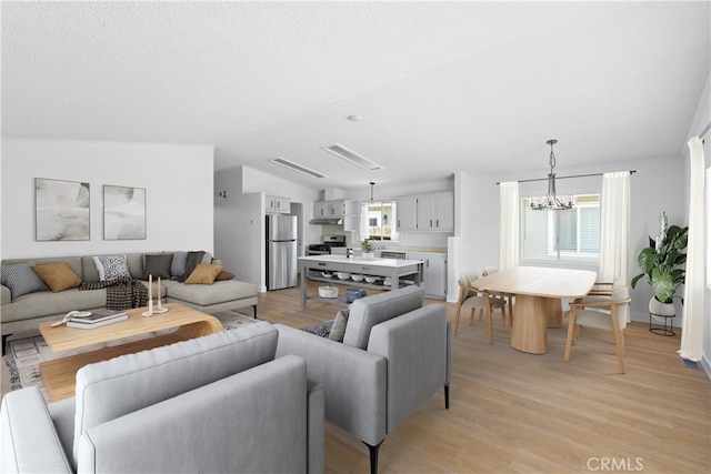 living area featuring lofted ceiling, a textured ceiling, a chandelier, and light wood-style floors