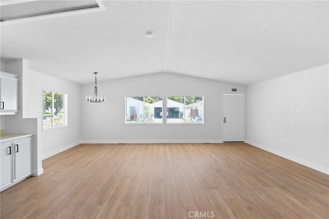 unfurnished living room with a chandelier, a wealth of natural light, vaulted ceiling, and light wood-style flooring