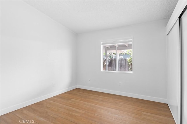 unfurnished bedroom featuring light wood-type flooring, a textured ceiling, baseboards, and a closet