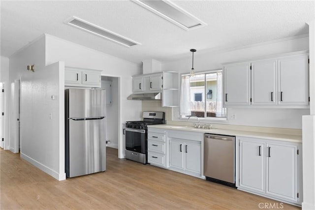 kitchen with lofted ceiling, under cabinet range hood, stainless steel appliances, a sink, and light wood-style floors