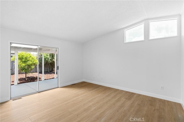 spare room with light wood-style floors, baseboards, visible vents, and vaulted ceiling