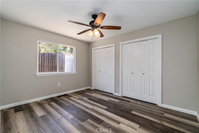 unfurnished bedroom with ceiling fan, two closets, and dark wood-type flooring