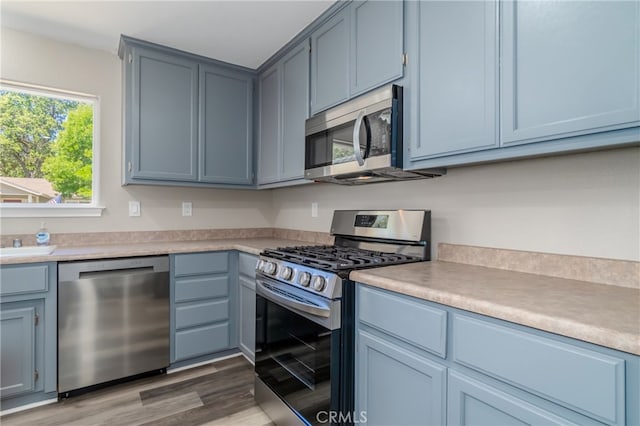 kitchen with blue cabinets, hardwood / wood-style floors, and stainless steel appliances