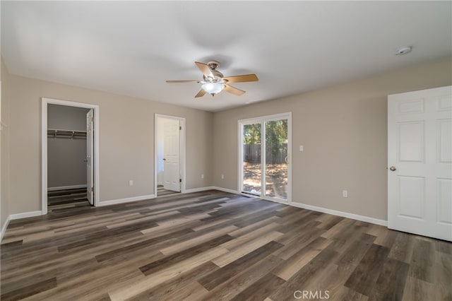 unfurnished bedroom with a spacious closet, dark wood-type flooring, access to exterior, a closet, and ceiling fan