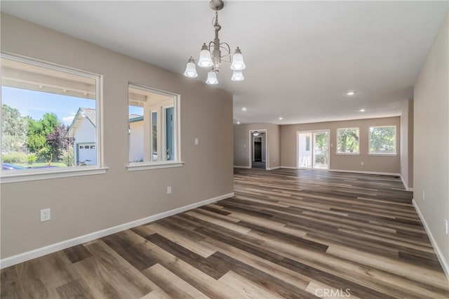 unfurnished living room featuring an inviting chandelier and dark hardwood / wood-style floors