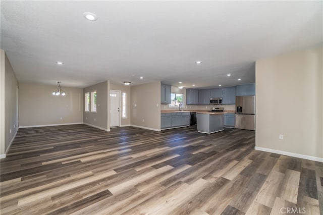 unfurnished living room featuring a chandelier, sink, a healthy amount of sunlight, and dark hardwood / wood-style flooring