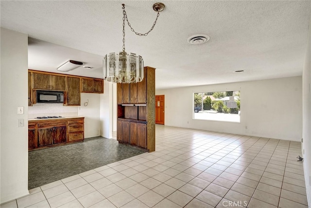 kitchen with light tile patterned flooring, a notable chandelier, a textured ceiling, and stainless steel gas cooktop