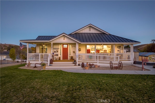 back house at dusk with covered porch and a lawn