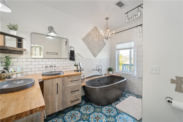 bathroom with vanity, tile patterned floors, a bathtub, a notable chandelier, and decorative backsplash