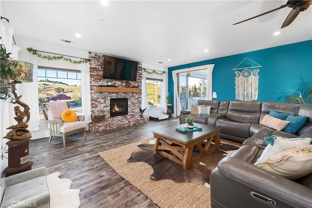 living room with ceiling fan, a large fireplace, and dark hardwood / wood-style flooring