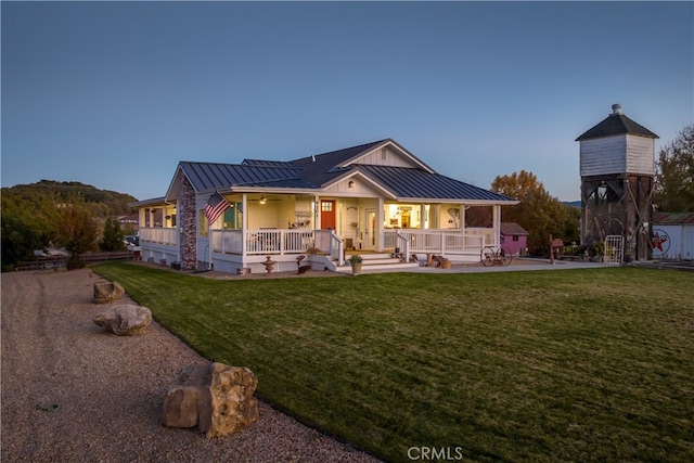 back house at dusk featuring covered porch and a yard