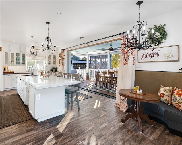 kitchen featuring dark hardwood / wood-style floors, backsplash, a center island with sink, pendant lighting, and white cabinets