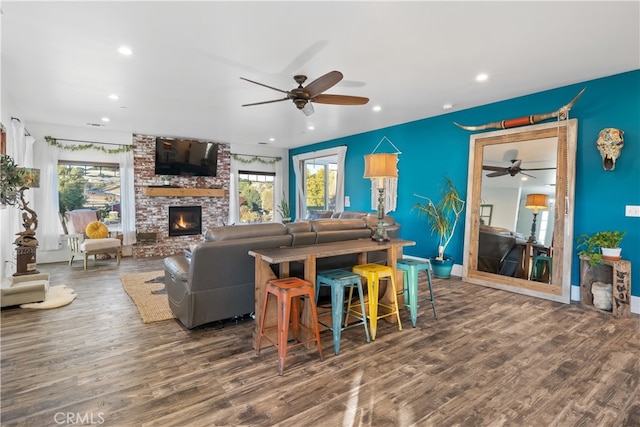 living room featuring a brick fireplace, dark wood-type flooring, and ceiling fan