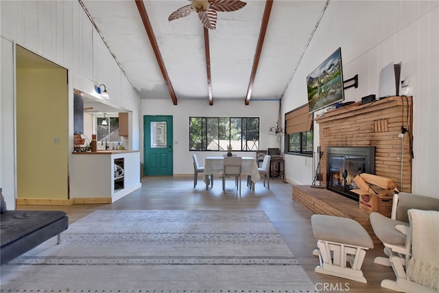 living room featuring high vaulted ceiling, a brick fireplace, beamed ceiling, wood-type flooring, and ceiling fan