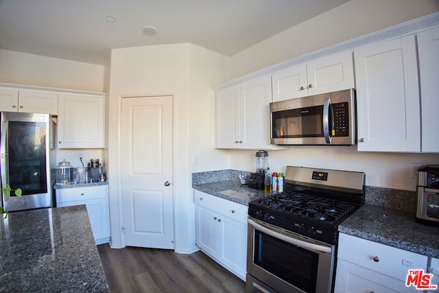 kitchen with dark wood-type flooring, appliances with stainless steel finishes, white cabinetry, and dark stone counters