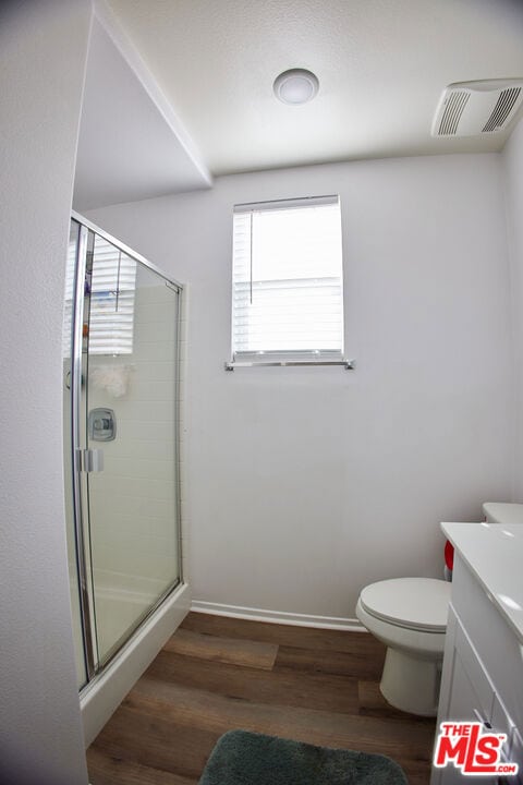 bathroom featuring vanity, hardwood / wood-style floors, a shower with shower door, and toilet